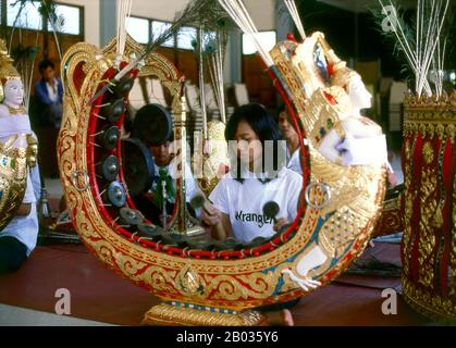 Thaïlande : une jeune femme joue du khong mon, un instrument de cercle de gong, dans un orchestre thaïlandais traditionnel, Bangkok. Le khong mon est un instrument de cercle de gong associé au peuple mon de l'Asie du Sud-est continentale. Il produit la même gamme d'emplacements que le cercle khong wong gong plus commun, mais plutôt que de reposer sur le sol, le cadre en bois du khong mon s'étend dans les airs en forme de fer à cheval. L'image d'un demi-homme, d'un demi-oiseau sculpté sur le cadre est traditionnelle et est censée symboliser un musicien céleste. Banque D'Images