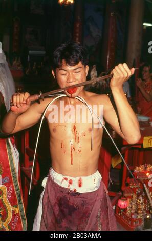 Thaïlande : un médium d'esprit possédé ou chanson de ma se coupe la langue avec une épée rouillée, le Festival des neuf dieux de l'empereur, Chao Mae Thapthim sanctuaire (maison taoïste chinoise de joss), Wang Burapha, Bangkok (1989). Le festival des neuf dieux de l'empereur est une célébration taoïste de neuf jours commençant à la veille du 9e mois lunaire du calendrier chinois, qui est observée principalement dans les pays d'Asie du Sud-est comme le Myanmar, Singapour, la Malaisie et la Thaïlande. Banque D'Images