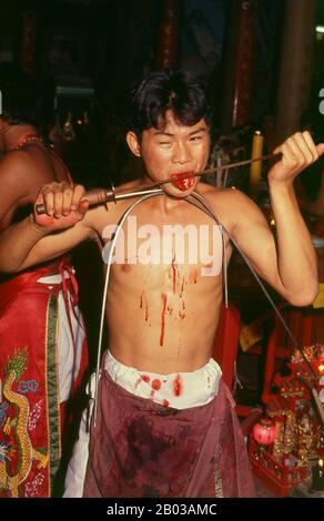 Thaïlande : un médium d'esprit possédé ou chanson de ma se coupe la langue avec une épée rouillée, le Festival des neuf dieux de l'empereur, Chao Mae Thapthim sanctuaire (maison taoïste chinoise de joss), Wang Burapha, Bangkok (1989). Le festival des neuf dieux de l'empereur est une célébration taoïste de neuf jours commençant à la veille du 9e mois lunaire du calendrier chinois, qui est observée principalement dans les pays d'Asie du Sud-est comme le Myanmar, Singapour, la Malaisie et la Thaïlande. Banque D'Images