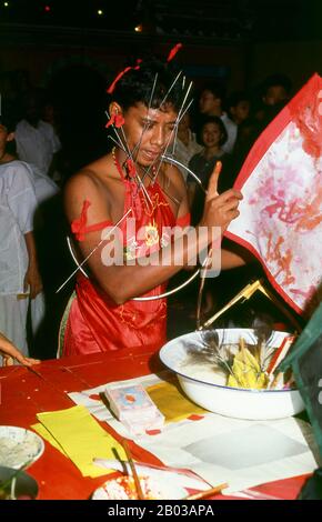 Thaïlande : un médium d'esprit possédé ou chanson ma avec piercings faciaux, le festival des neuf dieux de l'empereur, Chao Mae Thapthim Shrine (maison taoïste chinoise de joss), Wang Burapha, Bangkok (1989). Le festival des neuf dieux de l'empereur est une célébration taoïste de neuf jours commençant à la veille du 9e mois lunaire du calendrier chinois, qui est observée principalement dans les pays d'Asie du Sud-est comme le Myanmar, Singapour, la Malaisie et la Thaïlande. Banque D'Images