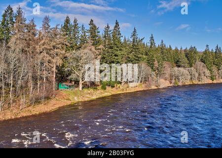 VILLAGE DE CARRON MORAY ECOSSE VUE SUR UNE CABANE DE PÊCHE VERTE ET LA RIVIÈRE DEPUIS LA ROUTE UNIQUE DE CARRON ET LE VIEUX PONT FERROVIAIRE QUI TRAVERSE LA RIVIÈRE SPEY Banque D'Images