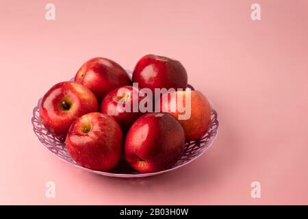 pommes rouges mûres rouges délicieux, gros plan dans un panier sur un fond rose. Banque D'Images