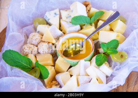 Assiette avec différents types de fromage sur papier blanc avec miel décoré de feuilles de menthe verte Banque D'Images