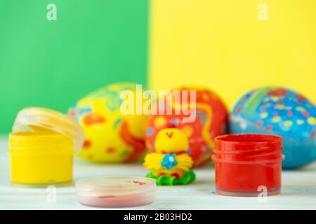 Image conceptuelle de Pâques avec du poulet de bébé à côté des œufs sur fond bleu en bois avec un espace publicitaire et de couleur rouge bleu vert jaune peinture avec pinceau Banque D'Images