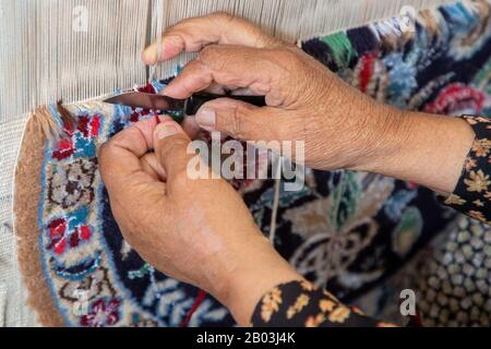 Femme a les mains de couper les fils dans le tissage de tapis, Iran Banque D'Images