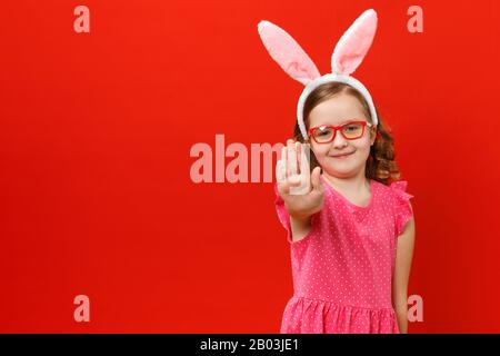 Petite fille dans les oreilles et les verres de lapin de pâques sur un fond rouge. L'enfant affiche un panneau d'arrêt. Banque D'Images