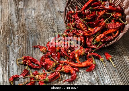 des piments rouges chauds secs sont strews d'un panier sur une table en bois ancienne Banque D'Images