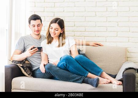 le temps est inestimable. jeune couple à la maison assis sur un canapé et regarder quelque chose au téléphone Banque D'Images