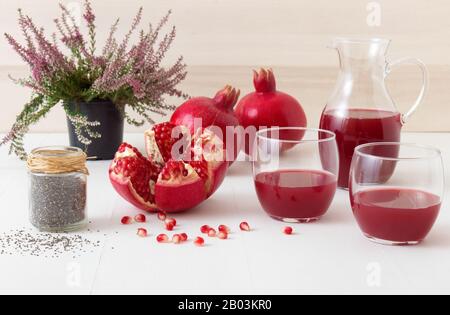 2 verres et pichet de jus de grenade frais, peu de grenades mûres avec un grenade partiellement pelée. Graines de grenade rouge et bocal de chia Banque D'Images