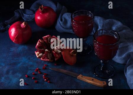 2 verres de jus de grenade frais avec peu de grenades mûres réelles sur fond bleu foncé. Grenade partiellement pelée, graines de rouge et kn peeling Banque D'Images