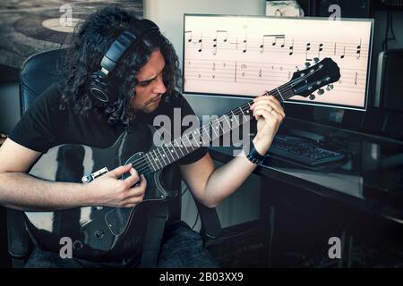 musicien de rock à poil long, homme avec casque, joue de la guitare électrique avec des partitions musicales sur fond d'écran Banque D'Images