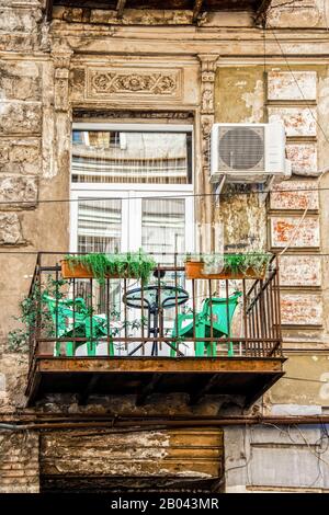 Balcon urbain - magnifique grunge - balcon rouillé à l'extérieur de l'ancien bâtiment européen avec des plantes et des chaises en plastique sous portail sculpté avec unité ac à s Banque D'Images