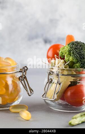 Capsules jaunes dans un pot en verre et légumes frais savoureux sur fond bleu. Nutrition multivitamines et supplément de légumes. Aliments biologiques inste Banque D'Images