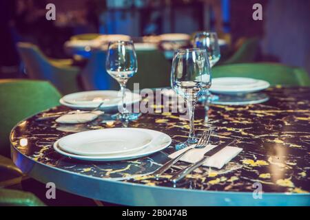 Table ronde en marbre. Chaise verte. Jeu de couteaux à couverts, cuillère, fourchette, plaque, verre à vin. Table en marbre noir . Banque D'Images