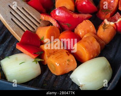 Les légumes frais sont cuits dans une poêle-grill, mélangés avec une spatule en bois. Carotte, poivron rouge doux, oignon. Le concept de nourriture végétarienne et saine. Banque D'Images