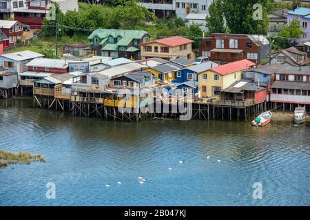 Vue sur les maisons sur pilotis (palafito) avec des cygnes à col noir (Cygnus melancoryphus) nageant sur l'eau dans la ville de Castro sur l'île de Chiloe au sou Banque D'Images