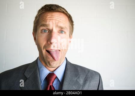 Homme d'affaires fatigué qui s'en tient à la langue avec une expression confuse Banque D'Images