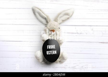 Lapin farci avec message 'Hapy Easter' en allemand sur fond de bois blanc Banque D'Images