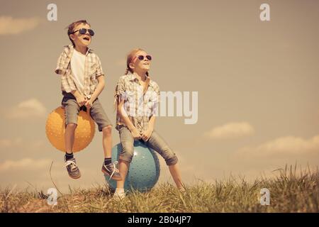 Frère et sœur jouant sur le terrain à la journée. Les enfants s'amuser en plein air. Ils sauter sur des ballons gonflables sur la pelouse. Concept d'ami Banque D'Images