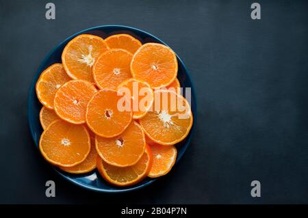 Des tangerines douces et juteuses fraîches, coupées sur une plaque sur fond sombre. Des aliments sains. Placer pour le texte. Banque D'Images