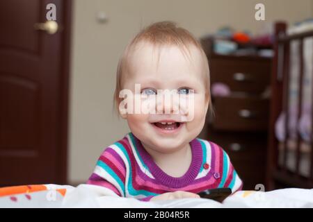 Petite fille souriante debout près du lit dans la chambre de lit Banque D'Images