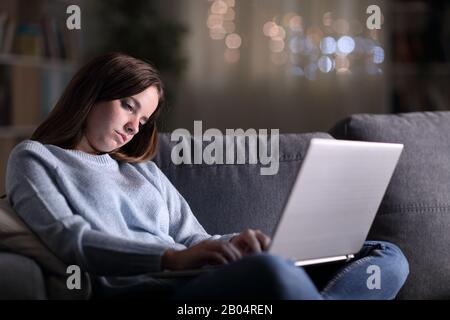 Femme endormie fatiguée utilisant un ordinateur portable tard dans la nuit assis sur un canapé à la maison Banque D'Images