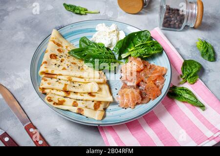 Délicieux petit déjeuner ou brunch - crêpes au saumon fumé, aux épinards et à la crème sure sur fond de béton. Banque D'Images