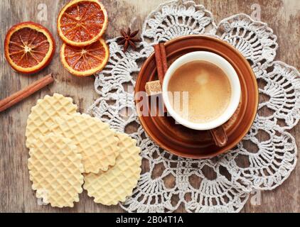 Une tasse de café, dentelle doily, orange confite, gaufres et bâtons de cannelle sur table en bois, style rustique. Mise au point sélective sur le café et les tons Banque D'Images