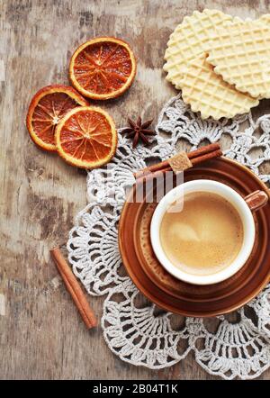 Une tasse de café, dentelle doily, orange confite, gaufres et bâtons de cannelle sur table en bois, style rustique. Mise au point sélective et tons/ Banque D'Images