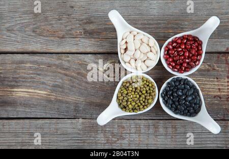 Ensemble de différentes variétés de haricots: Lima de bébé, petite noire, adzuki et mung dans des cuillères en céramique blanche (hors-d'œuvre) sur fond de bois, foc sélectif Banque D'Images