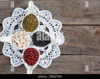 Ensemble de différentes variétés de haricots: Lima de bébé, petite noire, adzuki et mung dans des cuillères en céramique blanche (hors-d'œuvre) sur fond de bois, foc sélectif Banque D'Images