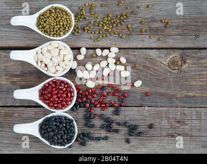 Ensemble de différentes variétés de haricots: Lima de bébé, petite noire, adzuki et mung dans des cuillères en céramique blanche (hors-d'œuvre) sur fond de bois, foc sélectif Banque D'Images