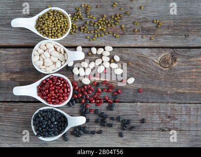 Ensemble de différentes variétés de haricots: Lima de bébé, petite noire, adzuki et mung dans des cuillères en céramique blanche (hors-d'œuvre) sur fond de bois, foc sélectif Banque D'Images