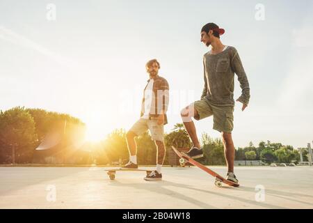 Les jeunes s'entrainrent avec un long-board avec lumière du soleil dans le dos - Skaters amis en plein air dans la ville urbaine avec des planches à roulettes - sport extrême et un conceps d'amitié Banque D'Images