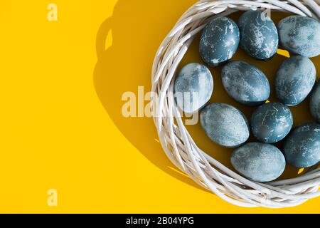 Oeufs de Pâques de couleur bleue texturés dans un nid ou une couronne sur un fond jaune brillant de vacances. Concept de vacances de printemps. Copyspace. Pose plate. Haut Banque D'Images