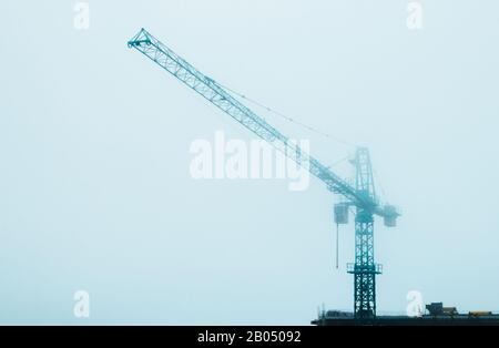 Grue de construction de tour dans le ciel bleu de la ville brumeuse le jour nuageux. Banque D'Images