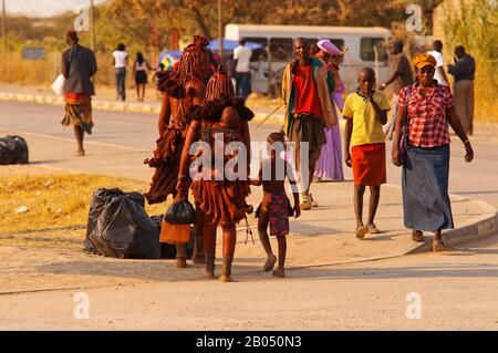 Himbas dans les ornements tribaux traditionnels et une femme d'Herero sur des vêtements verts marchant dans les rues d'Outjo, Namibie Banque D'Images