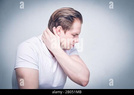 Un homme dans un T-shirt blanc souffre de pincer son cou et son joint. Vous avez mal à la tête. Tons. Gros plan. Banque D'Images