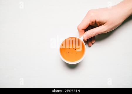 La main de l'homme tient un mug avec thé sur un fond en bois blanc avec espace de copie. Vue de dessus. Coose vers le haut. Banque D'Images
