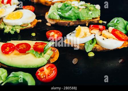Toasts de patate douce avec avocat, œufs durs, tomates et graines de sésame sur fond sombre. Concept de repas sain. Cuisine propre, plats du Pescetarian, vue sur le dessus Banque D'Images