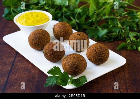 Falafel végétalien placé sur un plateau de service blanc. Sauce tahini avec poudre de curcuma et quelques feuilles de persil dans un fond flou. Banque D'Images