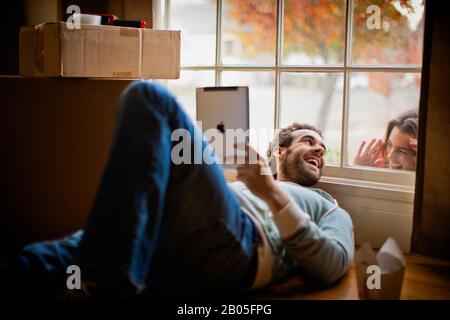 Homme de milieu d'adulte surpris par sa femme tout en couché sur le sol et en utilisant sa tablette numérique. Banque D'Images