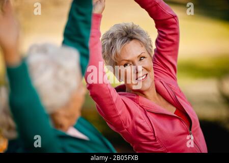 Deux smiling senior woman doing stretching exercices ensemble dans un parc. Banque D'Images