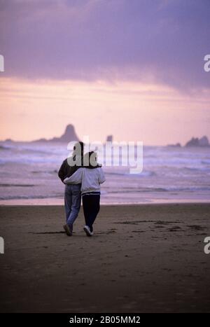 ÉTATS-UNIS, OREGON, CANNON BEACH, COUPLE MARCHANT LE LONG DE LA PLAGE EN SOIRÉE LUMIÈRE Banque D'Images