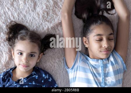 Deux jeunes filles noires, sœurs, se trouvent au lit dans une embrasse sur le dos. Des filles persanes sur le lit avec un téléphone. Enfants du Moyen-Orient. Banque D'Images