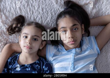 Deux jeunes filles noires, sœurs, se trouvent au lit dans une embrasse sur le dos. Des filles persanes sur le lit avec un téléphone. Enfants du Moyen-Orient. Banque D'Images