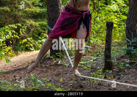 Une vue rapprochée sur les jambes d'une personne luttant pour l'équilibre lors d'une performance de corde à desserrer dans la nature, avec la corde raide attachée aux arbres dans une forêt Banque D'Images