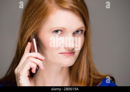 REDEHEAD Femme sur téléphone Curieux ou Confus Regarder l'appareil photo Banque D'Images