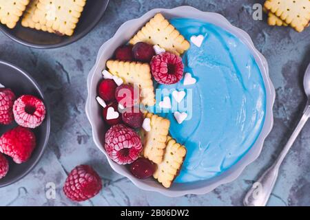 Bol à smoothie aux fruits teint avec de la poudre de spiruline bleu naturel saine et recouvert de framboises rouges, de canneberges et de petits biscuits Banque D'Images