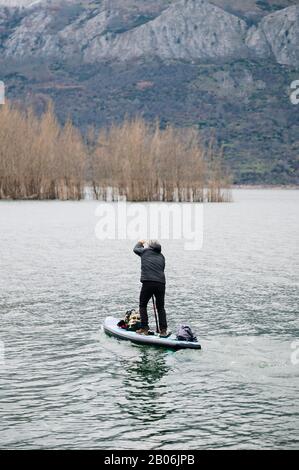 Un homme avec des vêtements chauds fait du paddle surf explorer dans un lac de montagne avec des bagages en haut de son conseil Banque D'Images